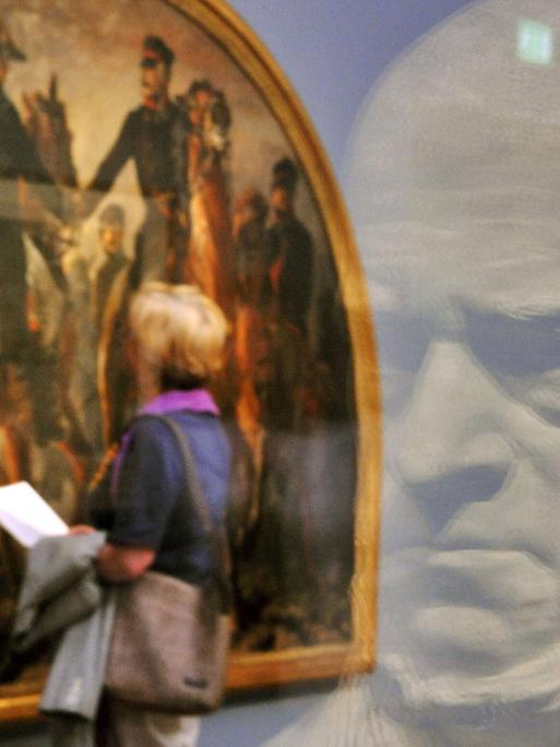 Eine Besucherin schaut sich das Gemälde "Blüchers Begegnung mit Wellington nach der Schlacht bei Belle-Alliance, 1858" von Adolph Menzel an. Im Vordergrund spiegelt sich die Gipsbüste Menzels, geschaffen von Reinhold Begas, in einer Glasscheibe.