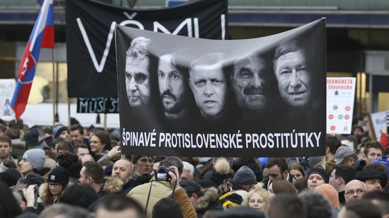 Demonstranten halten während einer Kundgebung gegen die Regierung und die Mafia unter dem Motto «Für eine anständige Slowakei» ein Plakat hoch. Zu sehen sind unter anderem die Gesichter von Ministerpräsident Fico (Mitte), Innenminister Kalinak (2.v.r) und Polizeichef Gaspar (rechts).  