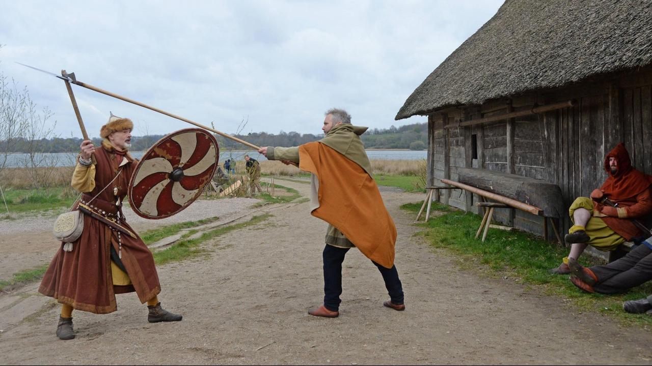 Zwei Wikinger-Darsteller im Wikingerdorf Haithabu kämpfen mit Speer, Axt und Schild gegeneinander.