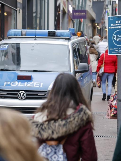 Passanten mit Schutzmasken beim Einkauf im Zentrum der Stadt Essen, links ein Polizeifahrzeug.