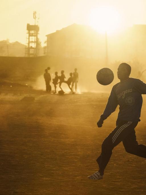 Jugendliche spielen im warmen abendlichen Gegenlicht Fußball in einem Slum Nairobis.