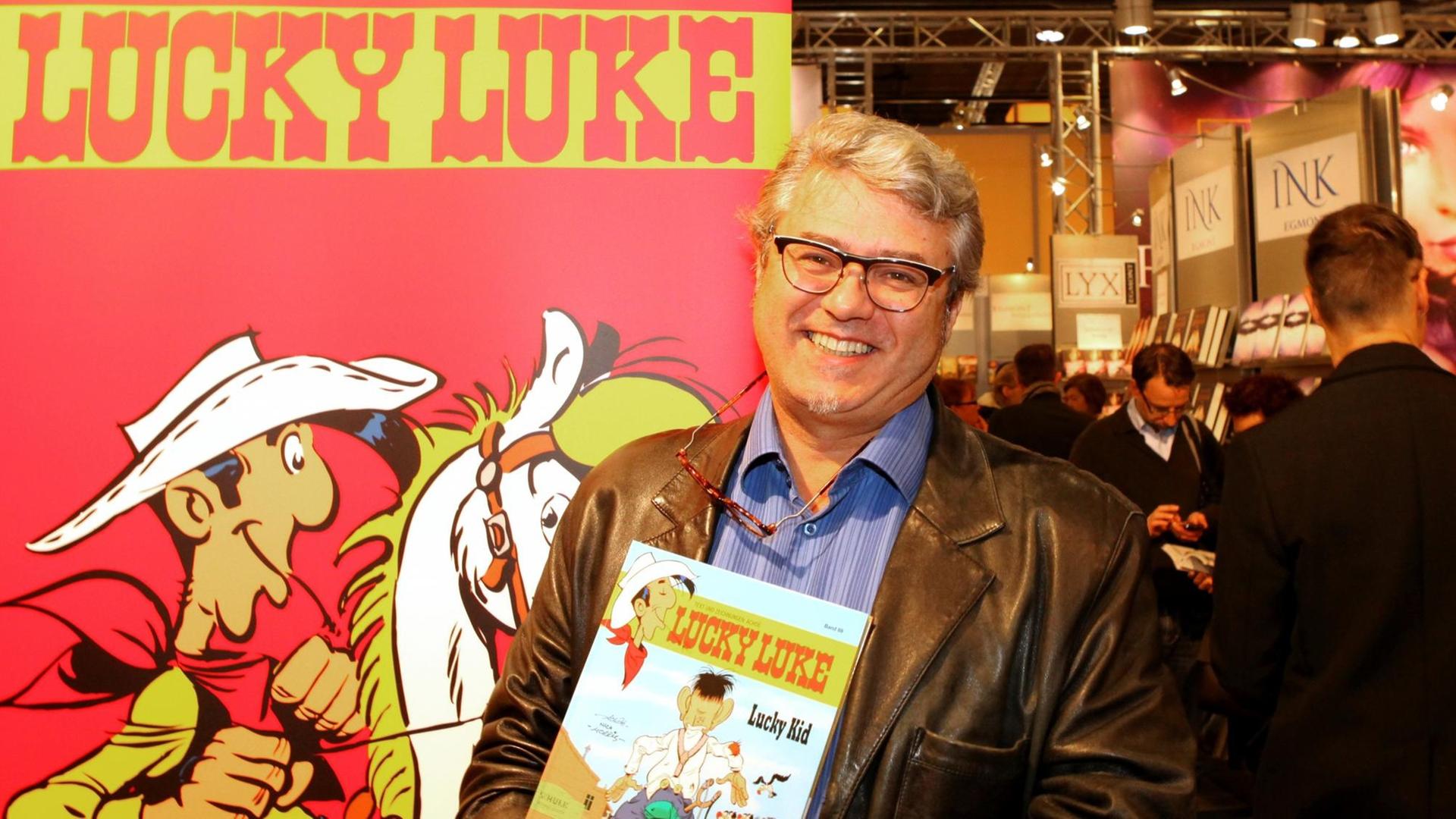 Der Lucky Luke Zeichner Achdé vor einem Plakat mit Lucky Luke.