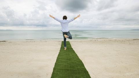 Ein Mann steht auf einem Bein auf einem grünen Teppich am Strand