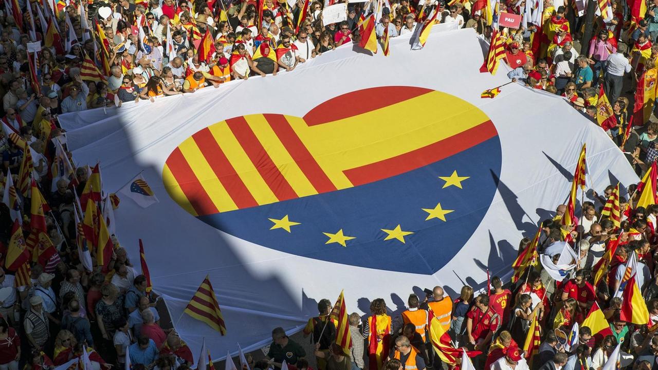 Ein Banner mit einem Herzen aus den Flaggen Kataloniens, Spaniens und Europas tragen Menschen bei dem Protest in Barcelona in Katalonien (Spanien) gegen die Pläne der Regionalregierung Katalonien zur Abspaltung von Spanien.