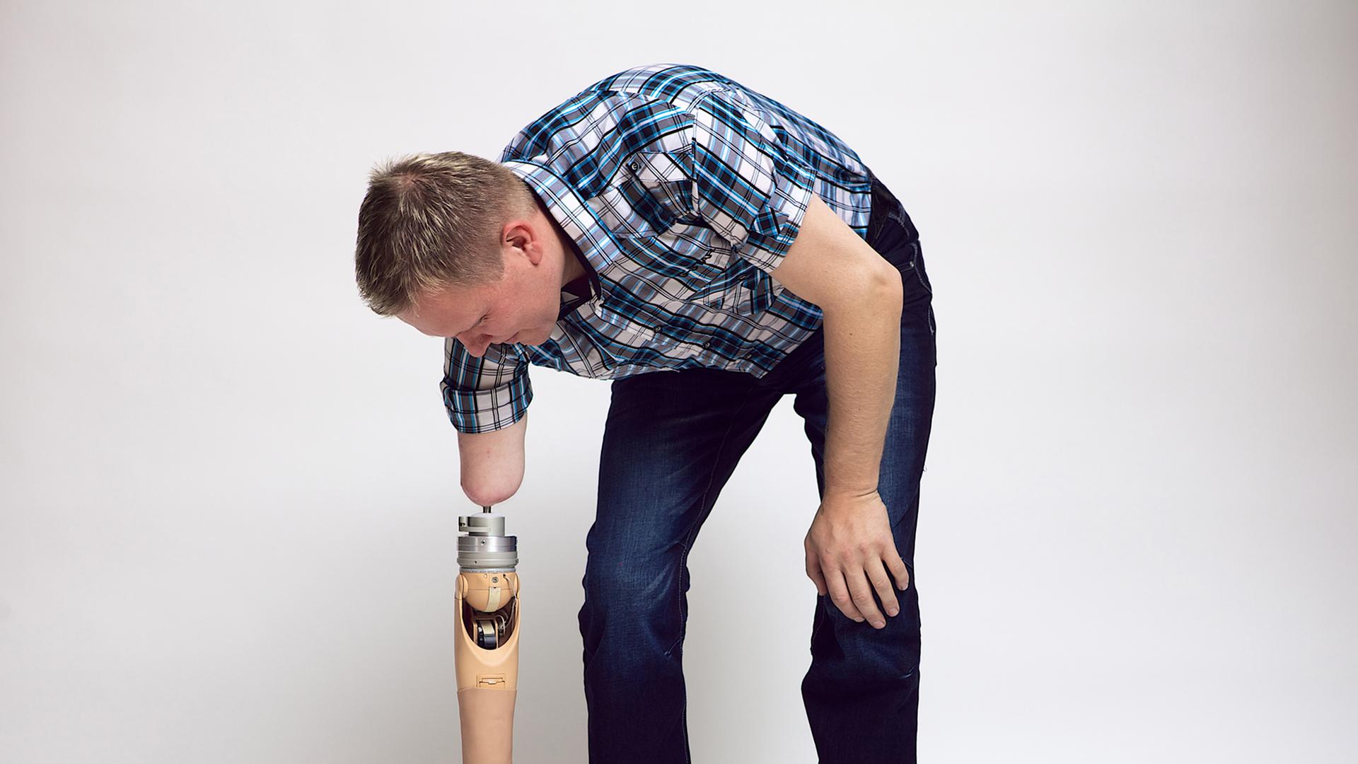 Ein Mann hebt mit einer Armprothese einen Ball vom Boden auf.