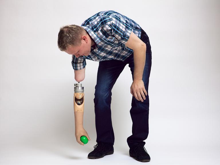 Ein Mann hebt mit einer Armprothese einen Ball vom Boden auf.