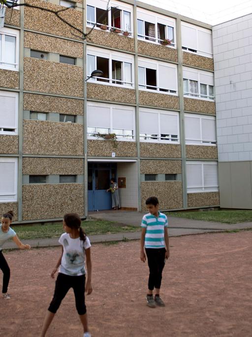 Anwohner und Journalisten stehen am 26.06.2015 vor dem Wohnhaus von Yassine S. - er hat kurz darauf gestanden, bei einem Terrorakt seinen Chef geköpft zu haben - in Saint Priest, Frankreich, während Jugendliche vor dem Gebäude Fußball spielen.