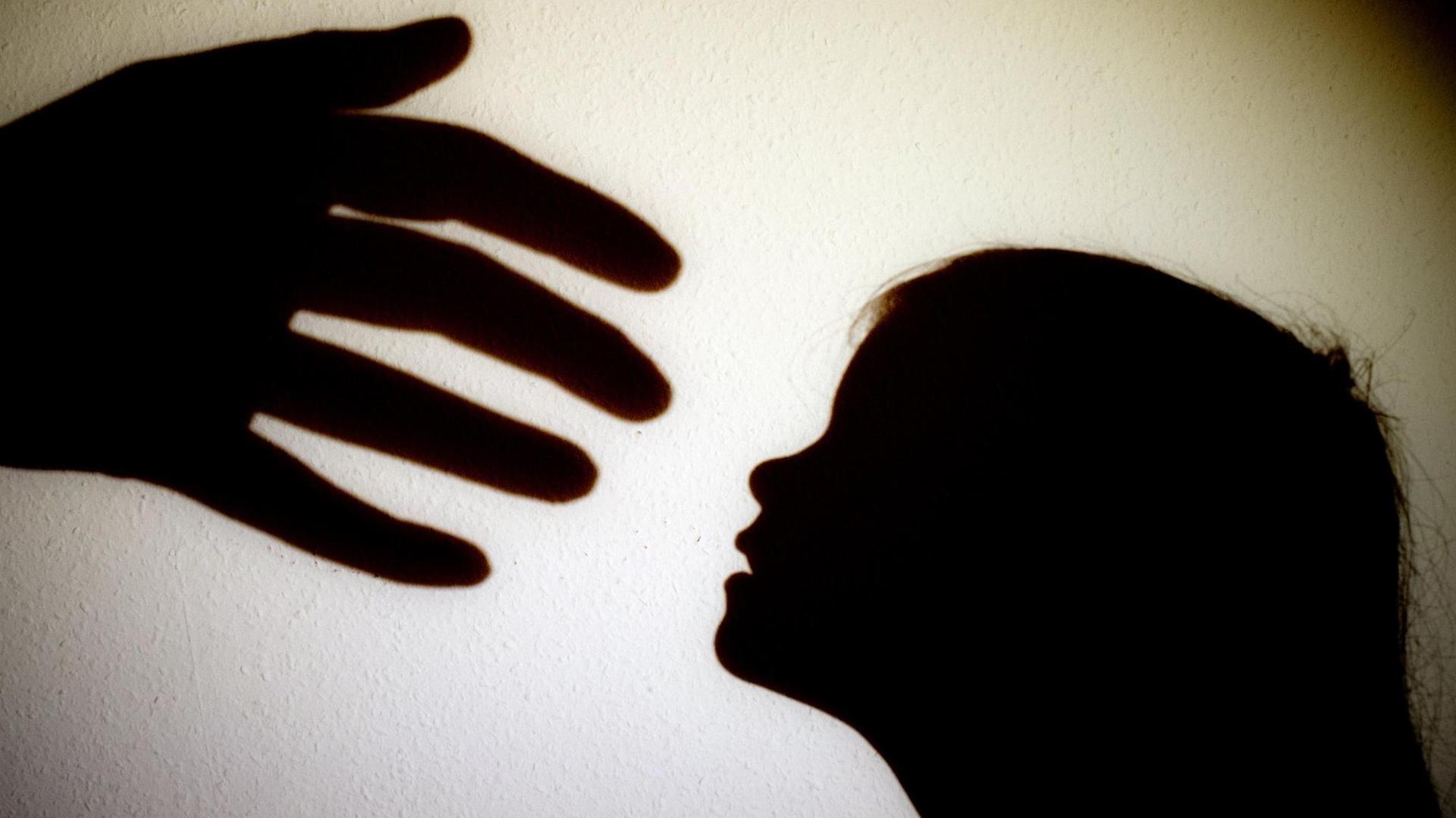 Schatten einer Hand einer erwachsenen Person und der Kopf eines Kindes an einer Wand eines Zimmers.
