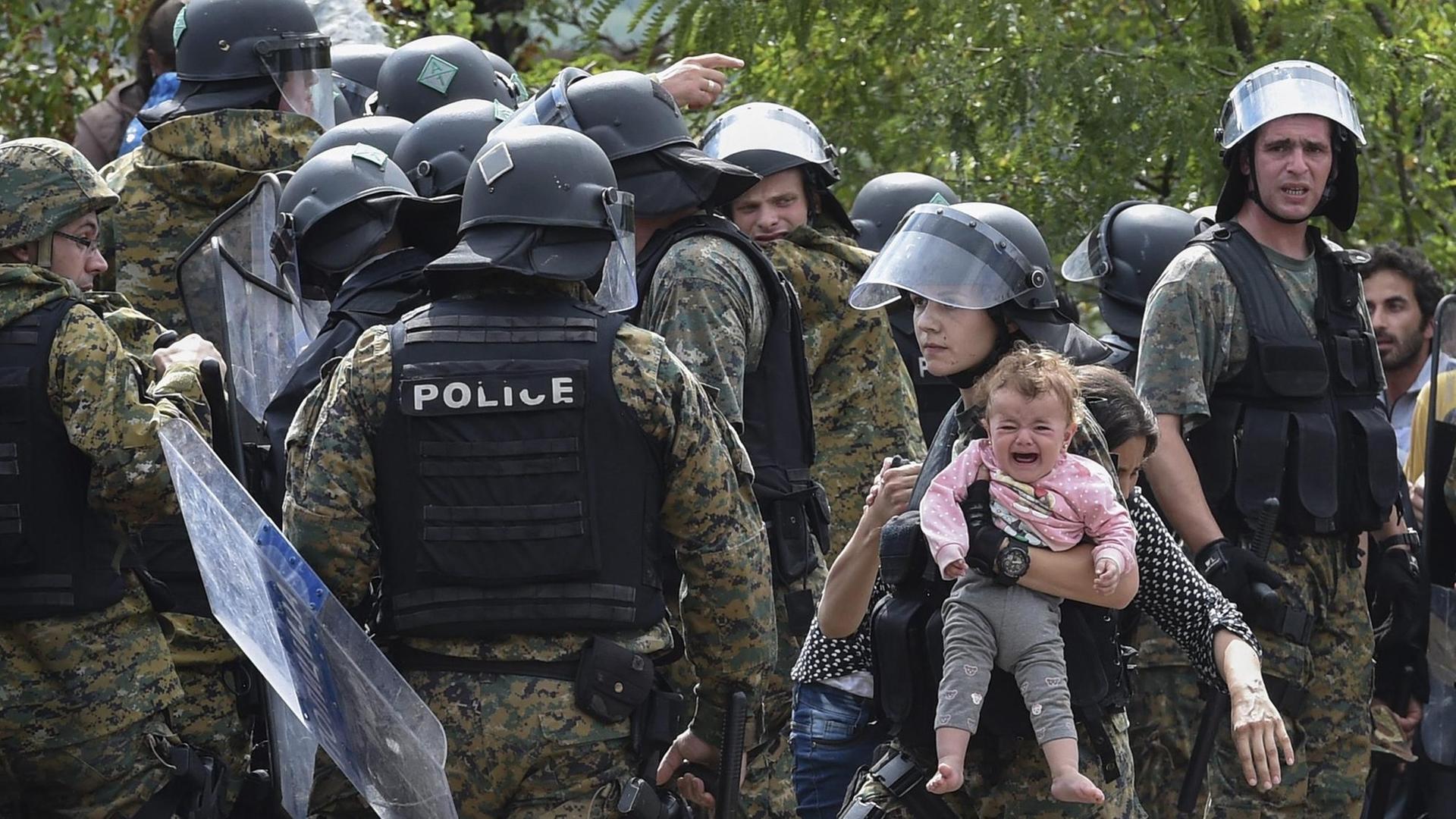 Ein Mitglied der mazedonischen Sondereinheit hält das Baby eines Flüchtlings.