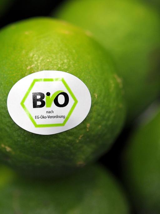 Zu sehen ist ein Haufen Limetten. Auf einer Limette befindet sich ein Aufkleber mit dem Bio-Siegel.