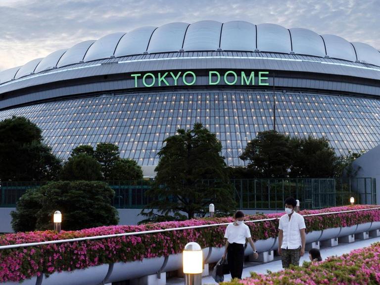 Das Baseball Stadion Tokyo Dome vor dem zwei Menschen mit Mundschutz laufen.