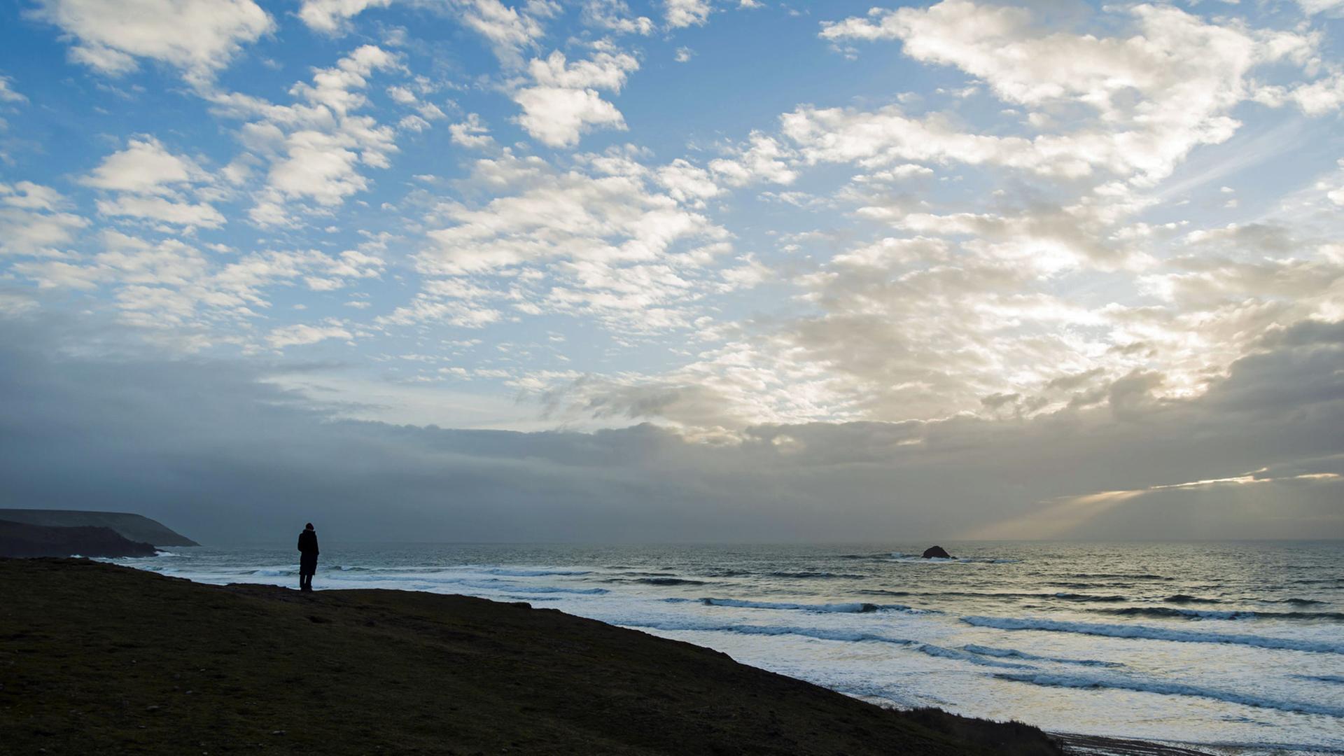 Ein Mensch steht vor einer Meereslandschaft mit Wolkenpanorama.
