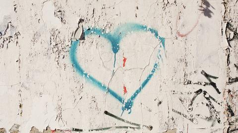 Die türkisfarbenen Umrisse eines Herzens sind auf eine Betonwand gemalt. 