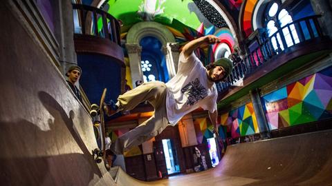 Eine leere Kirche beherbergt eine bunte Skaterbahn. Das Licht fällt durch die Kirchenfenster auf den Skater.