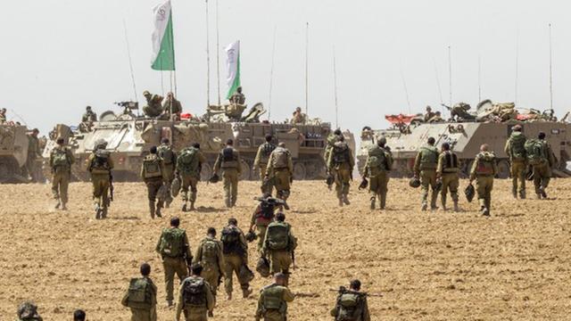 Israelische Soldaten laufen über ein Feld, im Hintergrund Panzer