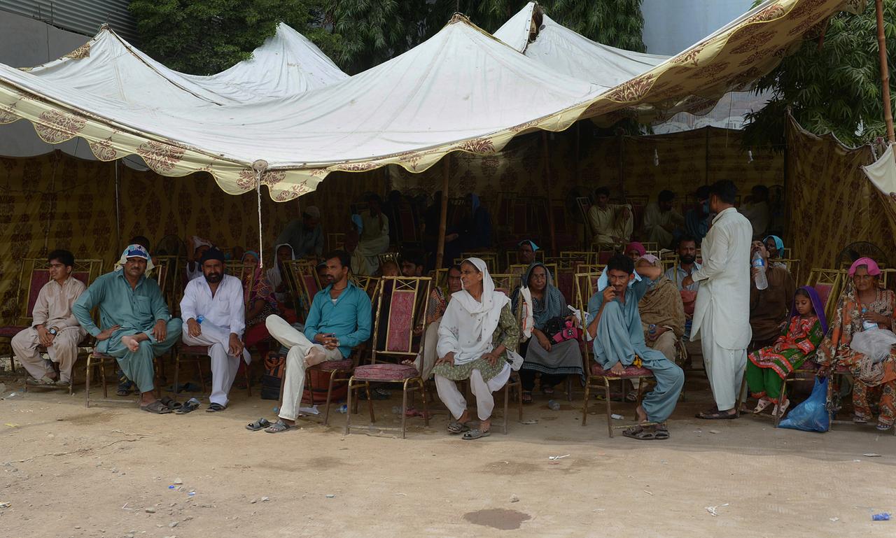 Pakistaner sitzen unter einem Sonnendach, um sich vor der Hitze zu schützen.