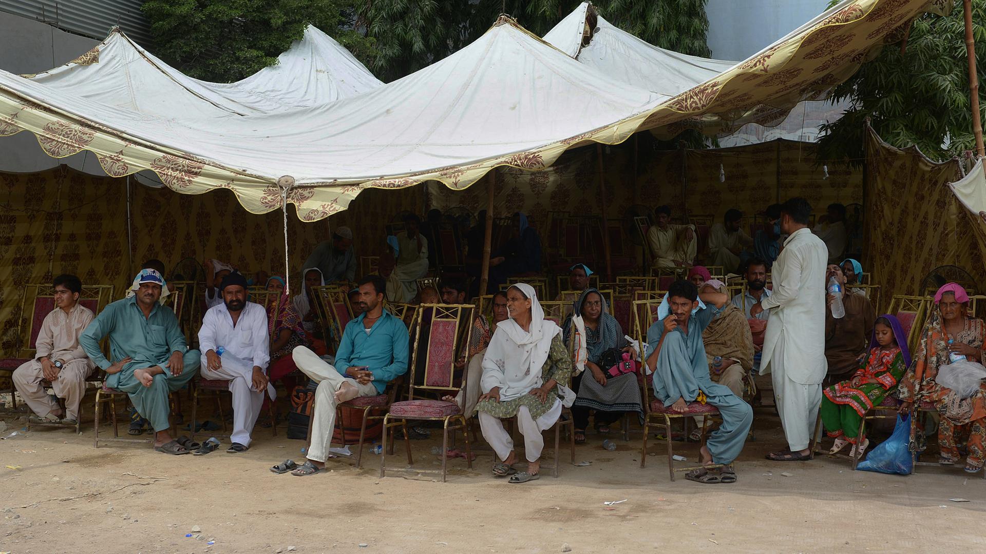 Pakistaner sitzen unter einem Sonnendach, um sich vor der Hitze zu schützen.