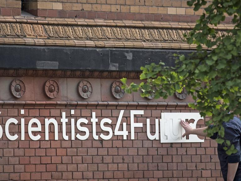 An einer Klinkerfassade in Berlin wird der Schriftzug "#Scientists4Future" angebracht.