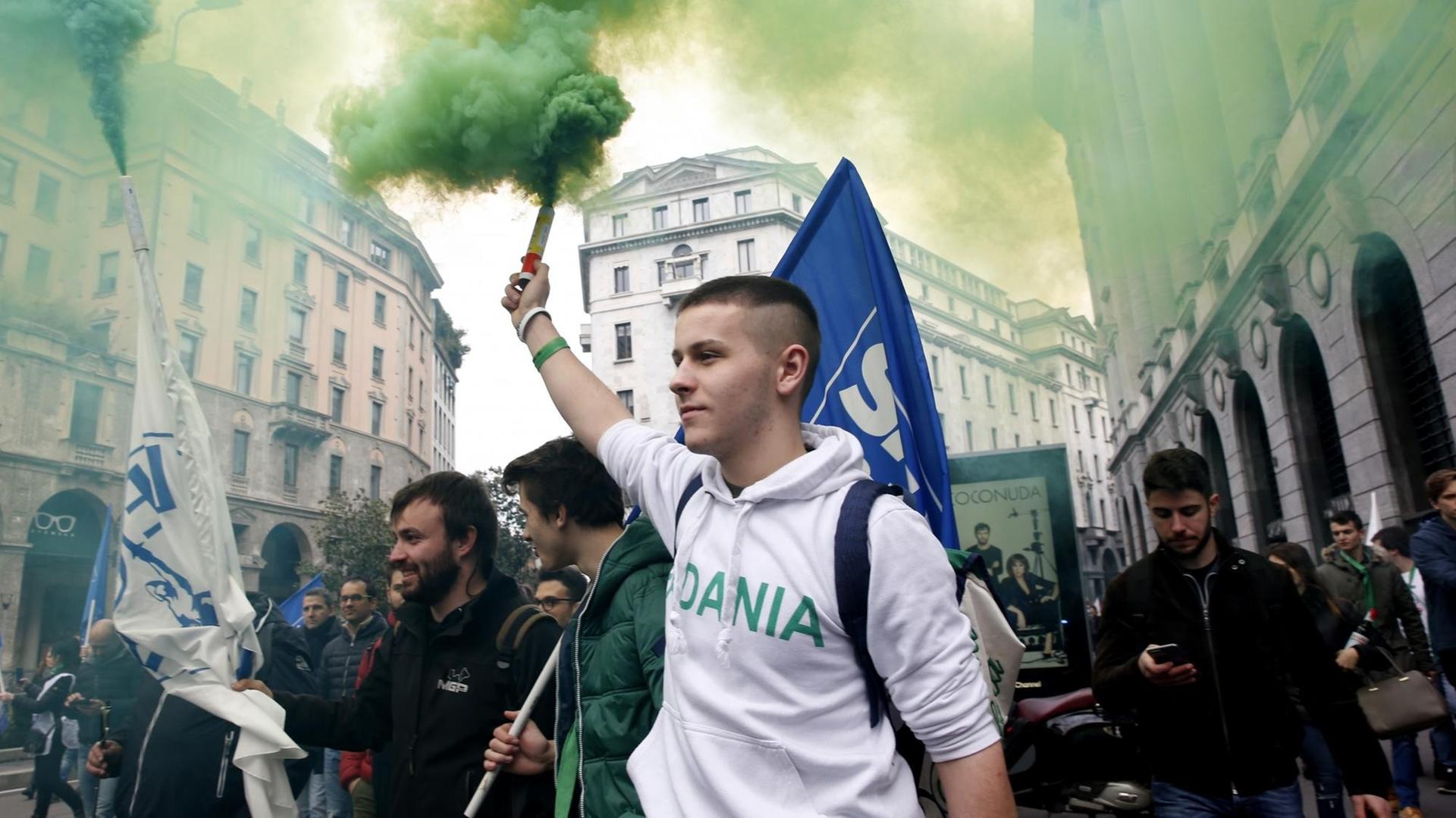 Ein junger Mann im Kapuzenpulli, ein Aktivist der rechtspopulistischen Partei Lega, hält bei einer Demonstration eine Rauchfackel in die Höhe. Im Hintgergrund Flaggen, Rauch und weitere Demonstranten.