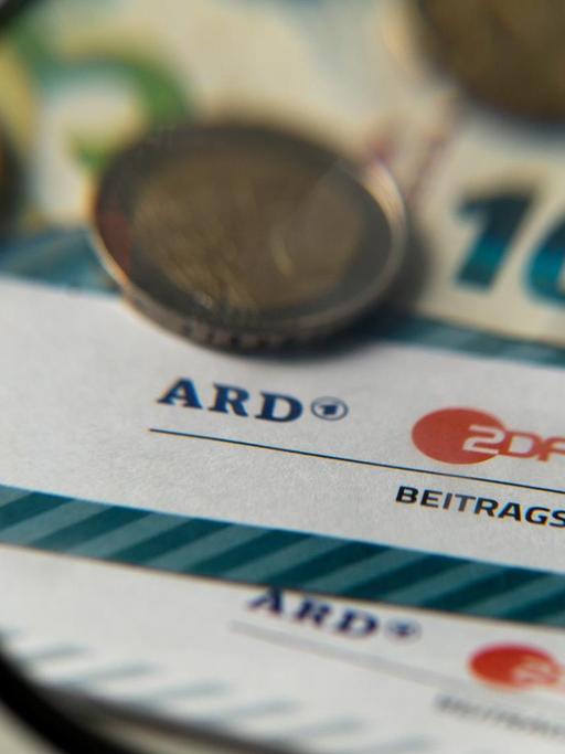 Auf einem Tisch liegt Münzgeld auf Formularen für Bürgerinnen und Bürger zu den Rundfunkbeiträgen ARD, ZDF und DRadio.