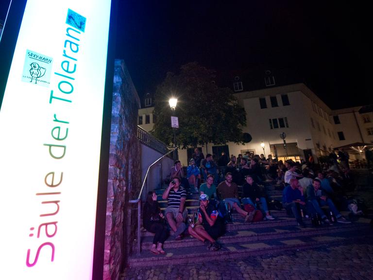 Menschen sitzen am 30.08.2014 auf dem Augustinerplatz in Freiburg (Baden-Württemberg) vor der Säule der Toleranz, die mit Farbenspielen den Lärmpegel visualisiert.