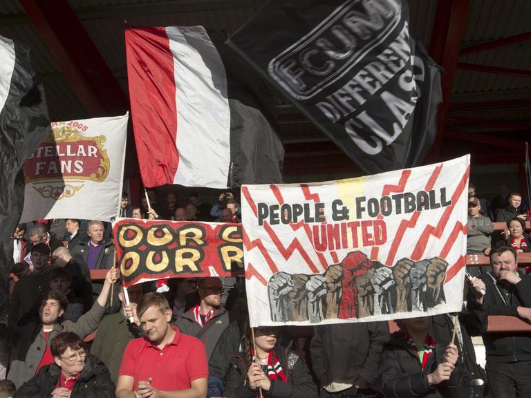 Fans von FC United of Manchester schwenken Banner im Broadhurst Park Stadion.