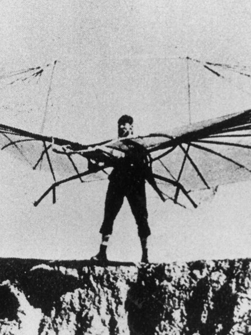 Otto Lilienthal bei einem seiner zahlreichen Gleitflugversuche. Er steht mit einem Gleitschirm auf vor einem Abhang