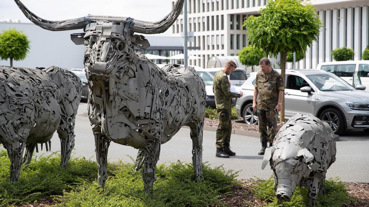 Bundeswehrangehörige stehen auf dem Betriebsgelände von Tönnies. Im Vordergrund Statuen von einem Stier und einem Schwein.  