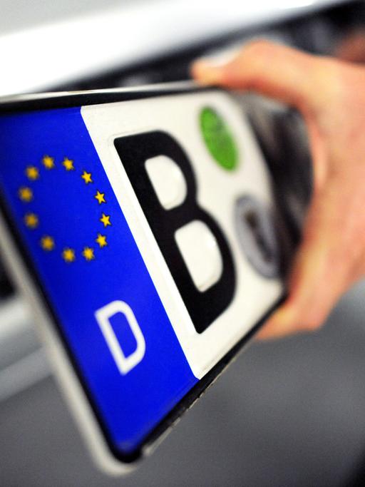 Ein Mann hat am Freitag in Berlin ein Nummernschild in der Hand, das er zuvor von einem Auto abmontiert hatte.
