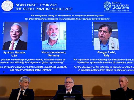 Das schwedische Nobelpreis-Komitee verkündet die Gewinner des Physik-Preises. Hinter ihnen ein Bildschirm mit den drei Gewinnern.