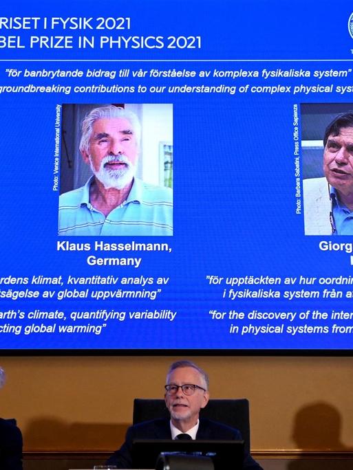 Das schwedische Nobelpreis-Komitee verkündet die Gewinner des Physik-Preises. Hinter ihnen ein Bildschirm mit den drei Gewinnern.
