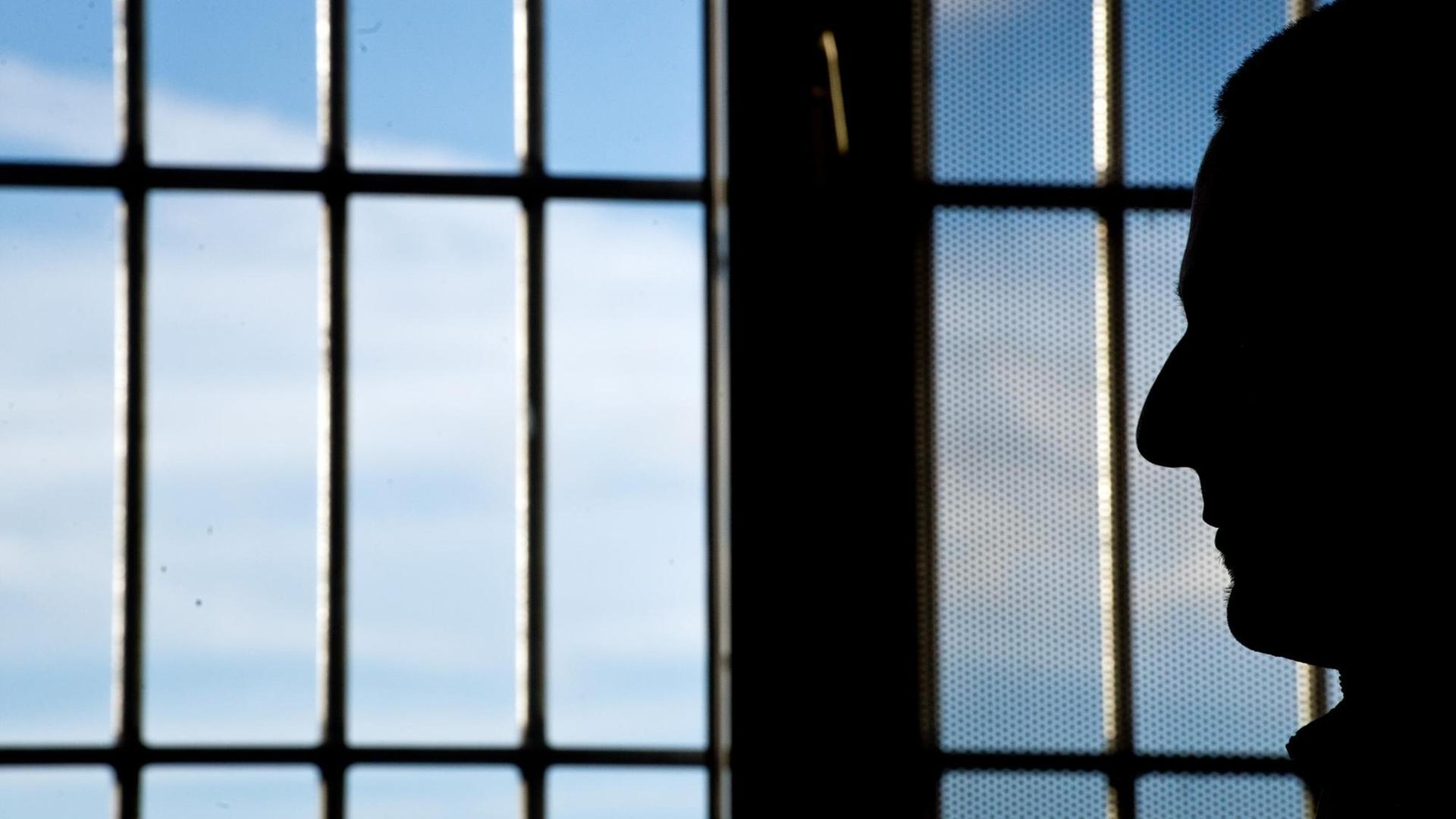 Ein Gefängnisinsasse sitzt vor einem vergitterten Fenster.