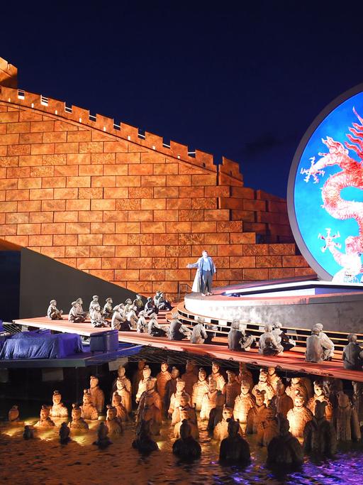 Sänger und Statisten treten vor der Kulisse der rot angestrahlten Chinesischen Mauer bei der Fotoprobe der Oper "Turandot" am 17.07.2015 auf der Seebühne in Bregenz in Vorarlberg (Österreich) auf