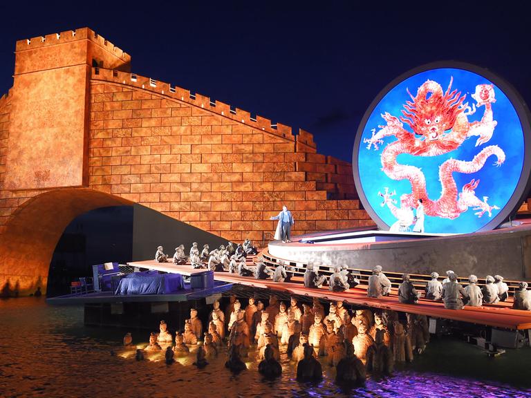 Sänger und Statisten treten vor der Kulisse der rot angestrahlten Chinesischen Mauer bei der Fotoprobe der Oper "Turandot" am 17.07.2015 auf der Seebühne in Bregenz in Vorarlberg (Österreich) auf. Die Premiere der Oper von Puccini ist am 22.07.2015.