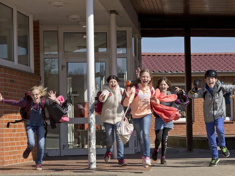 Glückliche Schüler laufen lachend nach Unterrichtsende aus einem Schulgebäude.
