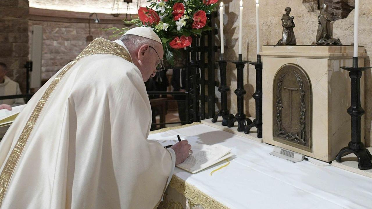 Der Papst steht gebeugt über einem Altar und unterzeichnet ein Dokument.