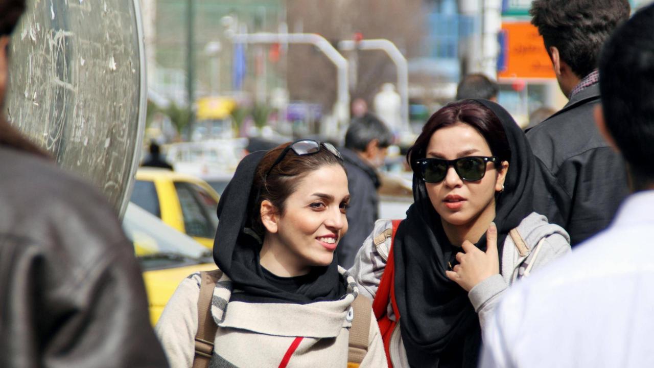 Zwei Frauen laufen in der iranischen Haupstadt Teheran mit wenig bedecktem Haar über die Straße.