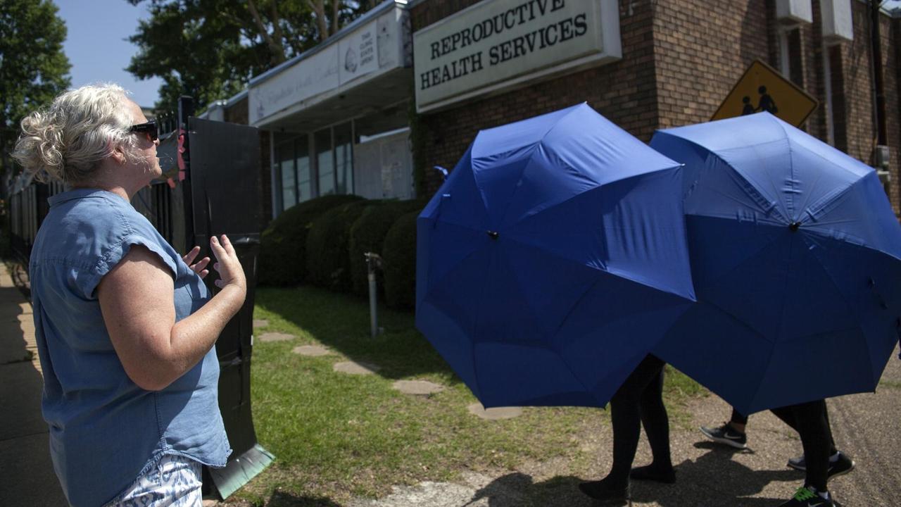 Zwei Schirme verdecken eine Patientin vor dem Gebäude mit der Aufschrift "Reproductive Health Services".
