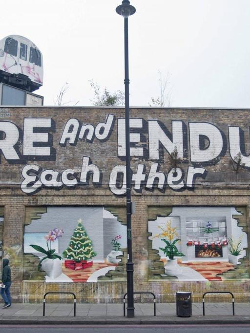 Menschen gehen im Londoner Stadtteil Shoreditch an einer mit Graffiti bemalten Hauswand vorbei. (Bild: Imago / United Archives International National News / Nick Edwards)