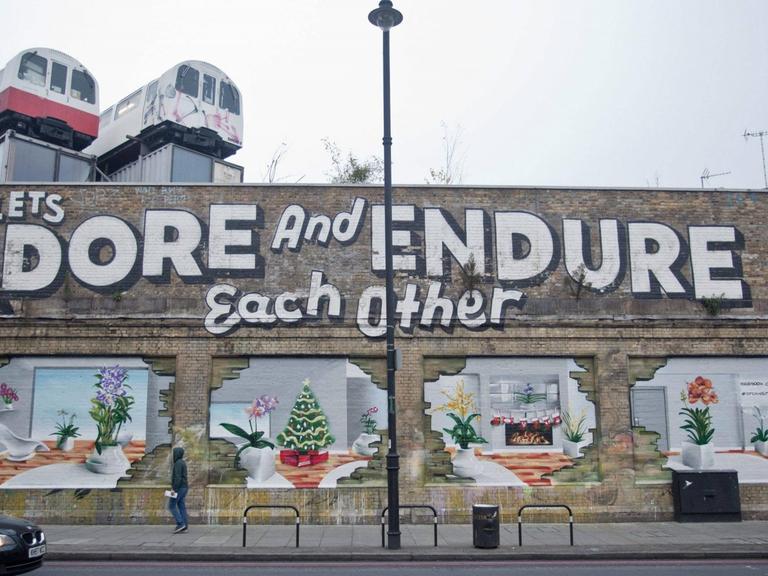 Menschen gehen im Londoner Stadtteil Shoreditch an einer mit Graffiti bemalten Hauswand vorbei. (Bild: Imago / United Archives International National News / Nick Edwards)