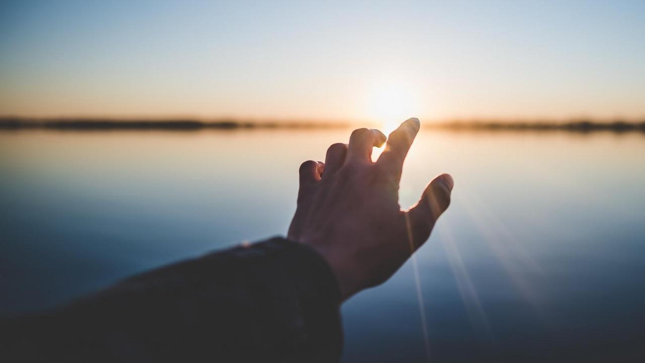 Eine Hand streckt sich in Richtung Horizont und Sonnenlicht.