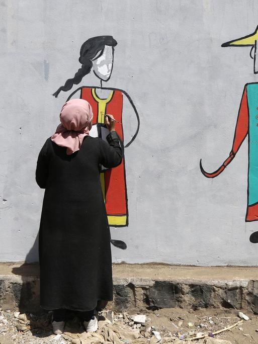 Eine Frau im Jemen malt zum Internationalen Frauentag ein Graffiti dreier Frauenfiguren an eine Wand.