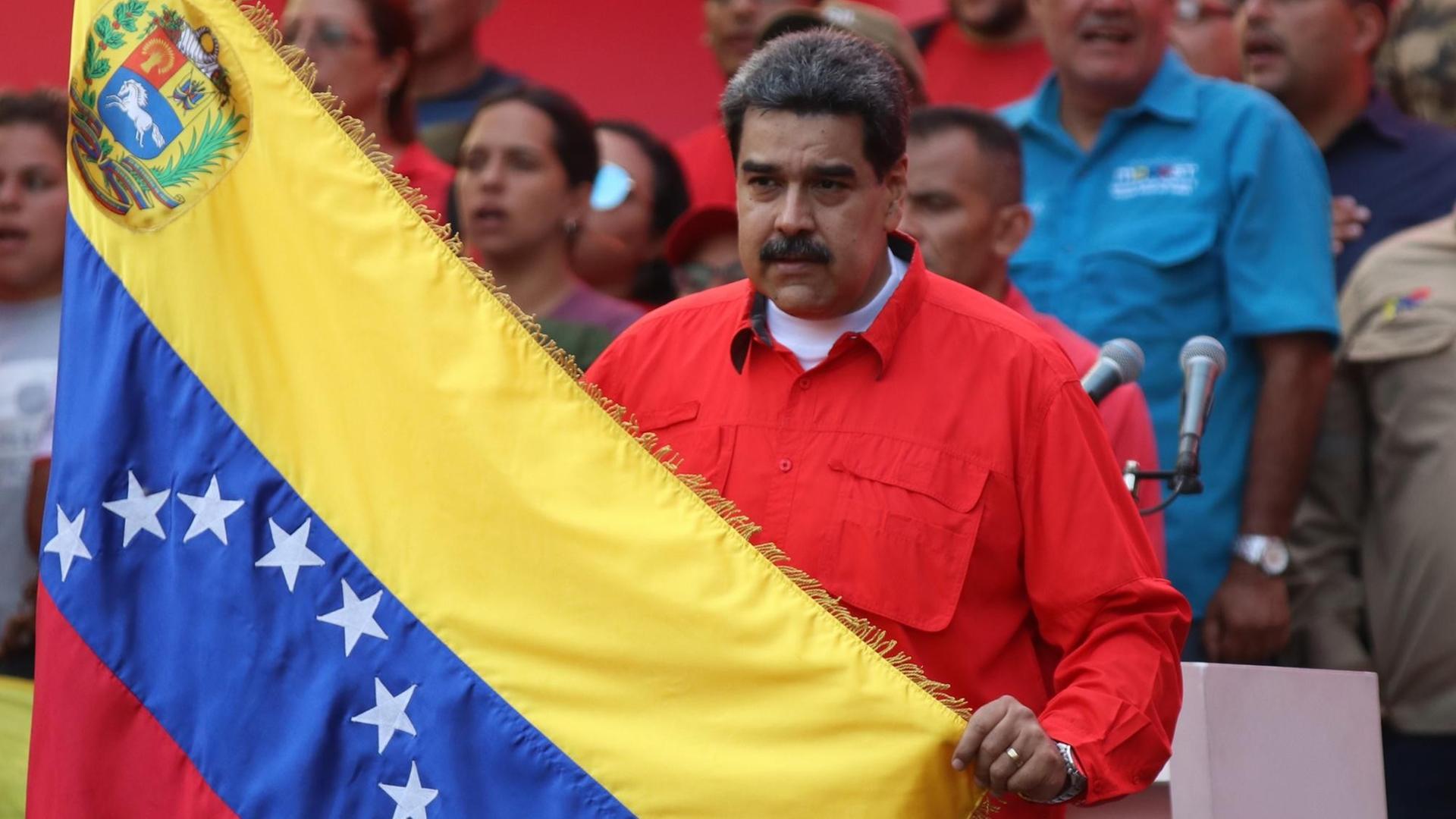 01.05.2019, Venezuela, Caracas: Nicolas Maduro (M), Präsident von Venezuela, hält während einer Kundgebung am Tag der Arbeit eine Flagge von Venezuela und singt die Nationalhymne.