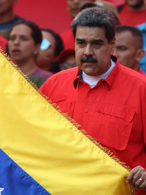 01.05.2019, Venezuela, Caracas: Nicolas Maduro (M), Präsident von Venezuela, hält während einer Kundgebung am Tag der Arbeit eine Flagge von Venezuela und singt die Nationalhymne.