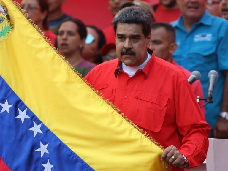 01.05.2019, Venezuela, Caracas: Nicolas Maduro (M), Präsident von Venezuela, hält während einer Kundgebung am Tag der Arbeit eine Flagge von Venezuela und singt die Nationalhymne.