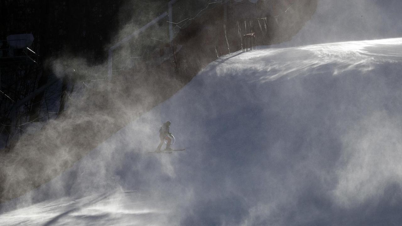 Ein Helfer auf Ski wird auf der Abfahrtstrecke von einer aufgewirbelten Schneewolke umweht.