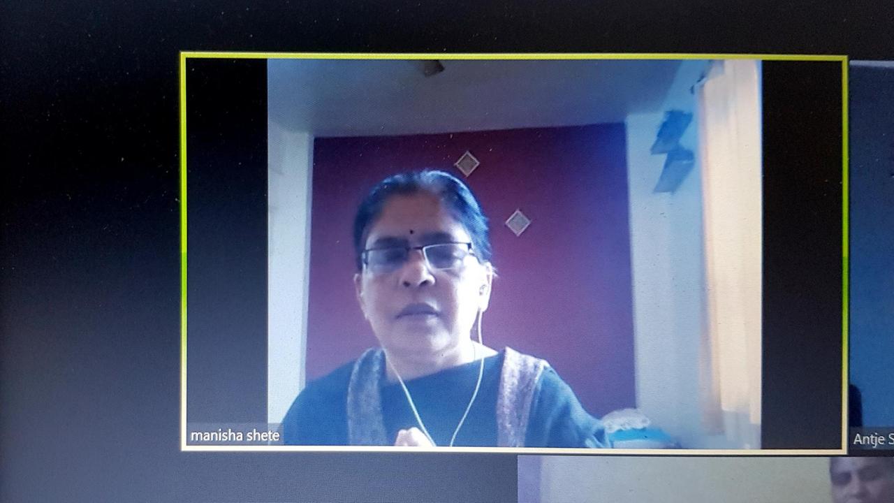 Auf einem Computerbildschirm ist eine indische Frau mit Brille bei einer Videokonferenz zu sehen.