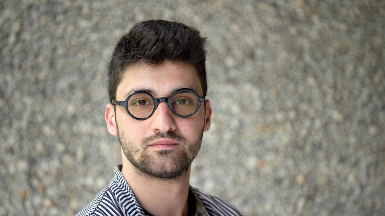 Der Regisseur Ersan Mondtag, aufgenommen vor einer grauen Steinwand