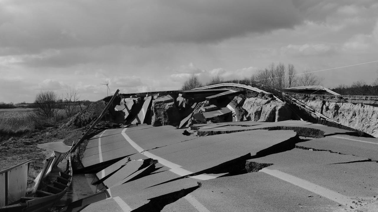 Zu sehen ist eine schwarz weiß Aufmahme einer kaputten Straße, mit stark aufgerissenem Asphalt. 