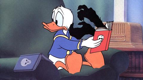 Donald Duck liest in einem Buch, aus dem ihm schwarze Hände entgegenkommen.